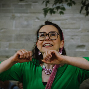 Erzählerin Tanja Schreiber mit langen schwarzen Haaren, Brille und in einem grünen Kleid erzählt Märchen bei einer Märchenwanderung
