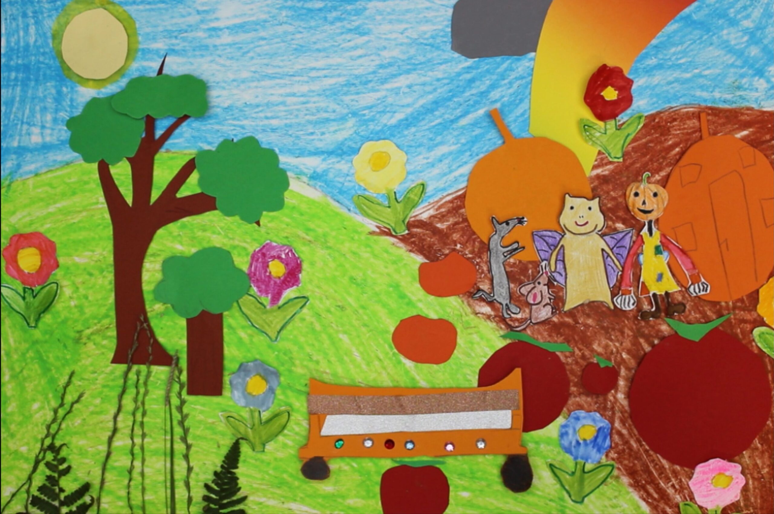 Kinderzeichnung zum Trickfilm Der goldene Drachenzahn. Zu sehen ist eine blühende Landschaft mit Bäumen, Blumen, Gräsern und Feldern. Am Himmel ist die Sonne, die kleine Regenwolke und ein Regenbogen zu sehen. Im Vordergrund sind die Held:innen der Geschichte zu sehen: die Hamsterdrachin Uschi, die Ratte Raffi, die Wühlmaus Willi und die Kürbisfee Kunigunde sowie das fliegende Kürbisauto.